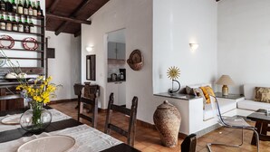 A dining area with a table set for two, a vase with flowers, and a shelf with bottles. - Villa Roberta at Costa Rei – Sardinian Beach Villa with Garden (Costa Rei)