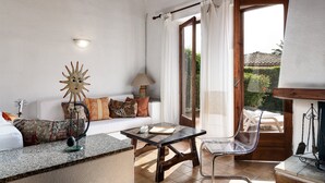 A room with a sofa, a table, a chair, a lamp, and a window with curtains. - Villa Roberta at Costa Rei – Sardinian Beach Villa with Garden (Costa Rei)