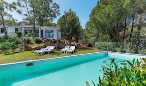 A swimming pool with two lounge chairs, a modern house, and surrounding trees.