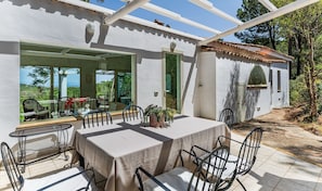 A covered patio with a table and chairs, a view of the outdoors, and a door leading to an interior space.