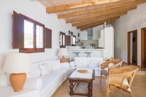 A spacious living area with a sofa, a coffee table, wicker chairs, a lamp, and a kitchen in the background. - Finca Fiori 2 – Peaceful Country House with Private Pool in Sardinia (S.Margh.di Pula)