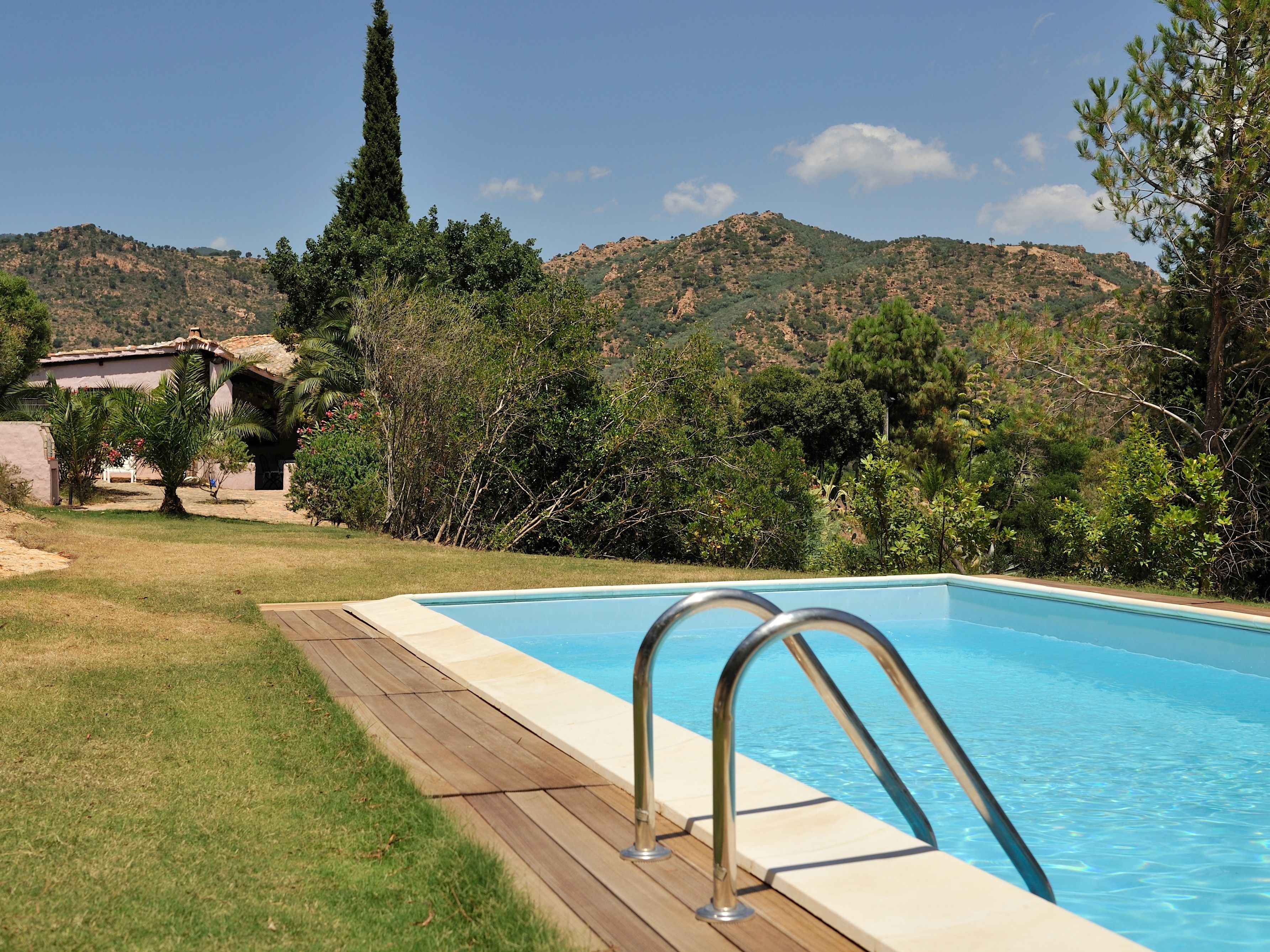 Una piscina con un solarium in legno, circondata da vegetazione e colline sullo sfondo.