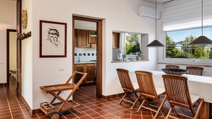 A modern kitchen with wooden cabinets, a dining area with a table and chairs, and a view of greenery outside. - Villa Aquila Giardino – Nature Retreat with Panoramic Views and Private Pool (S. Margh. di Pula)