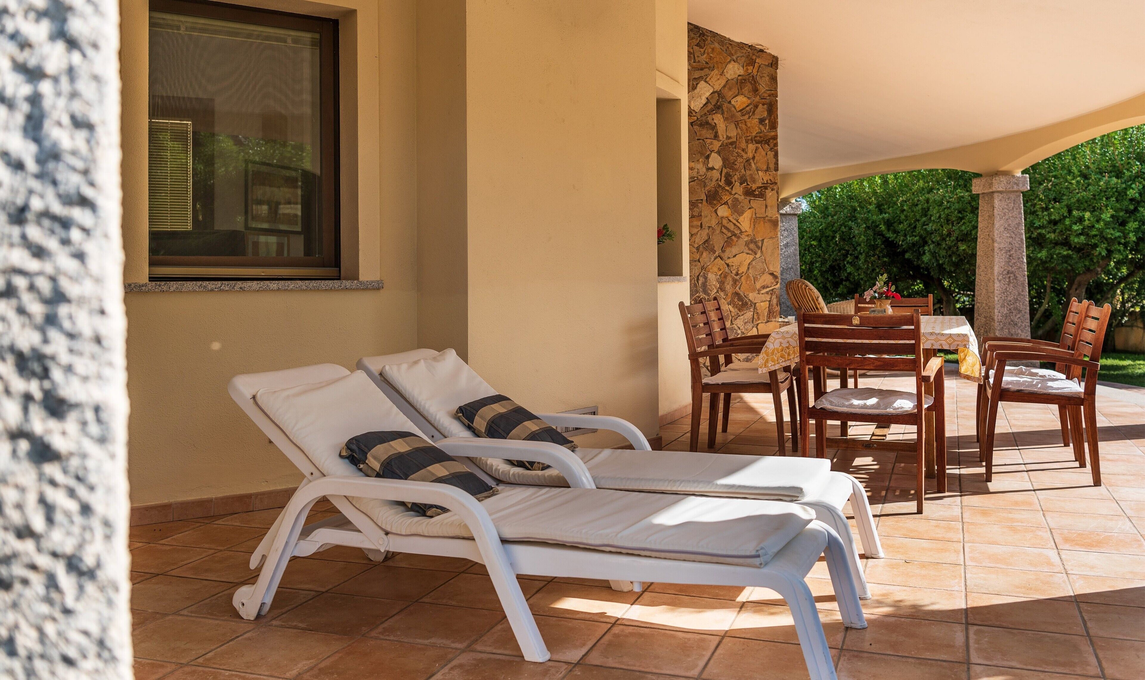 Un patio luminoso con due poltrone bianche, un pilastro in pietra e un tavolo con sedie.