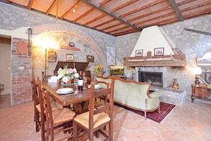A rustic dining area with a stone wall, wooden ceiling, and a fireplace. - Casale Mulino (Scansano)