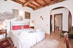 A bedroom with a bed, a nightstand, a lamp, a chair, and a door leading to another room. - Casale Mulino (Scansano)