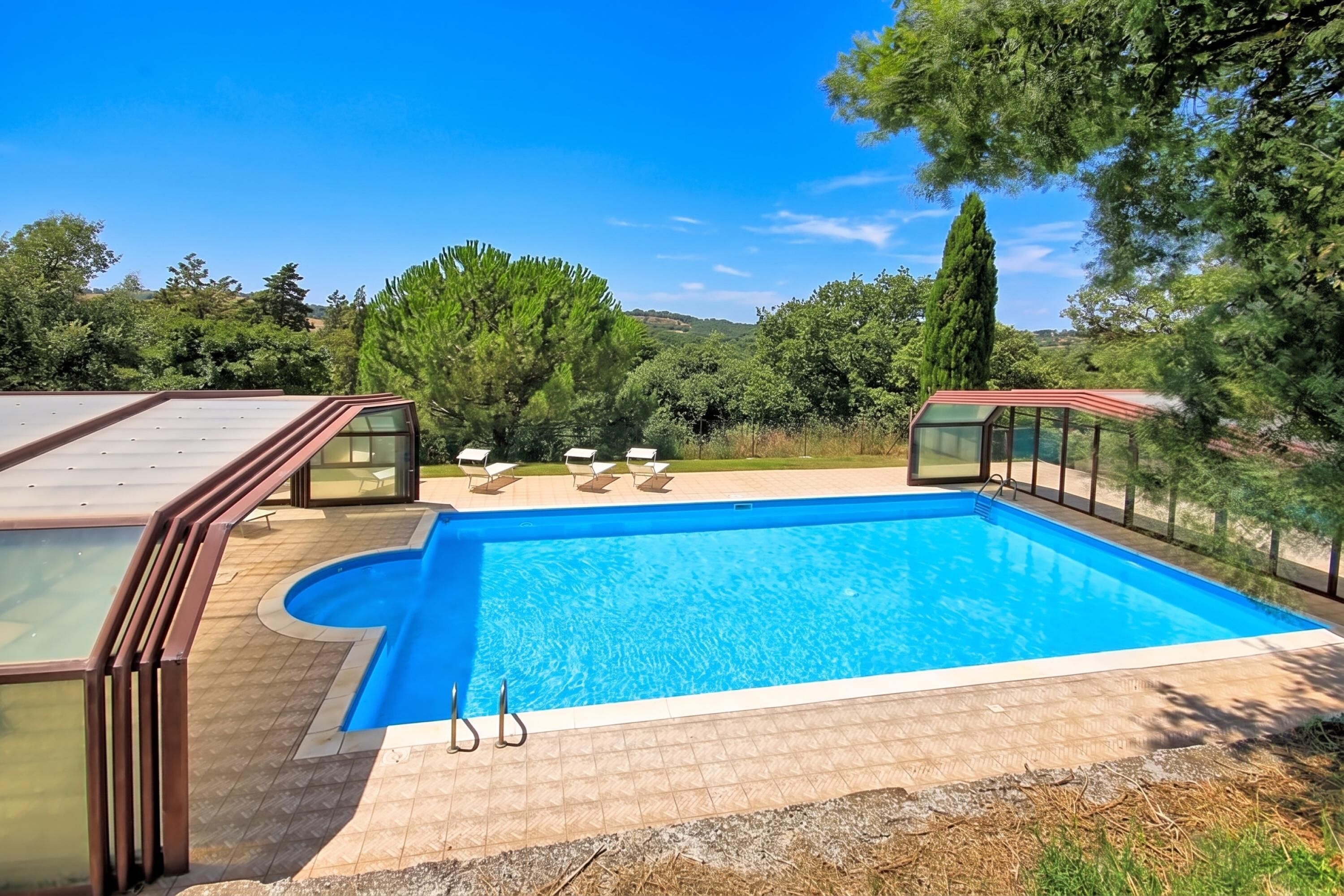 A swimming pool with a clear blue water, surrounded by a deck with lounge chairs.
