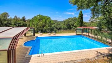 A swimming pool with a clear blue water, surrounded by a deck with lounge chairs.