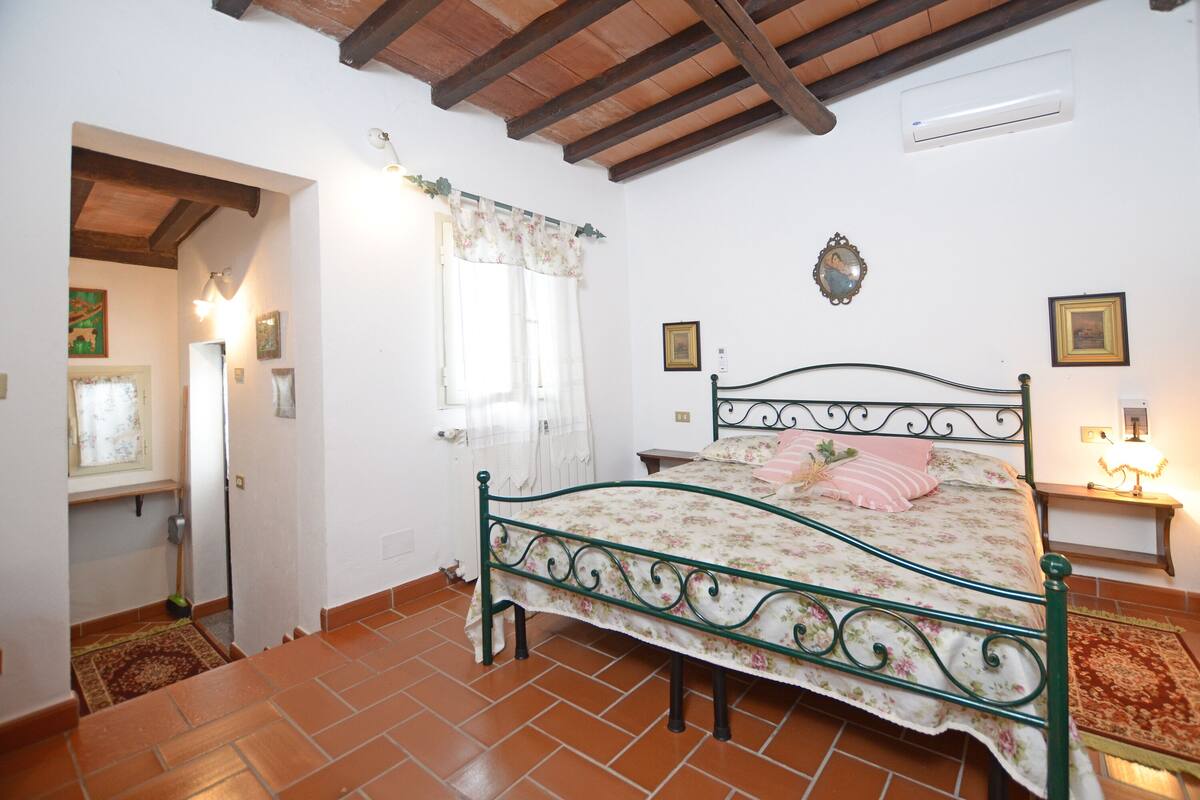 A bedroom with a bed, a window with curtains, a radiator, and a wall-mounted picture.