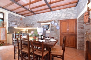 A rustic dining area with a stone wall, wooden ceiling beams, and a tiled floor. - Casale Mulino (Scansano)