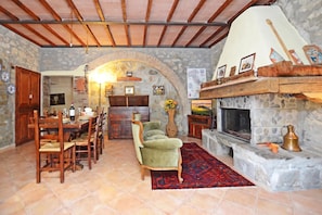 A rustic interior with a stone fireplace, wooden dining table, and a cozy seating area. - Casale Mulino (Scansano)