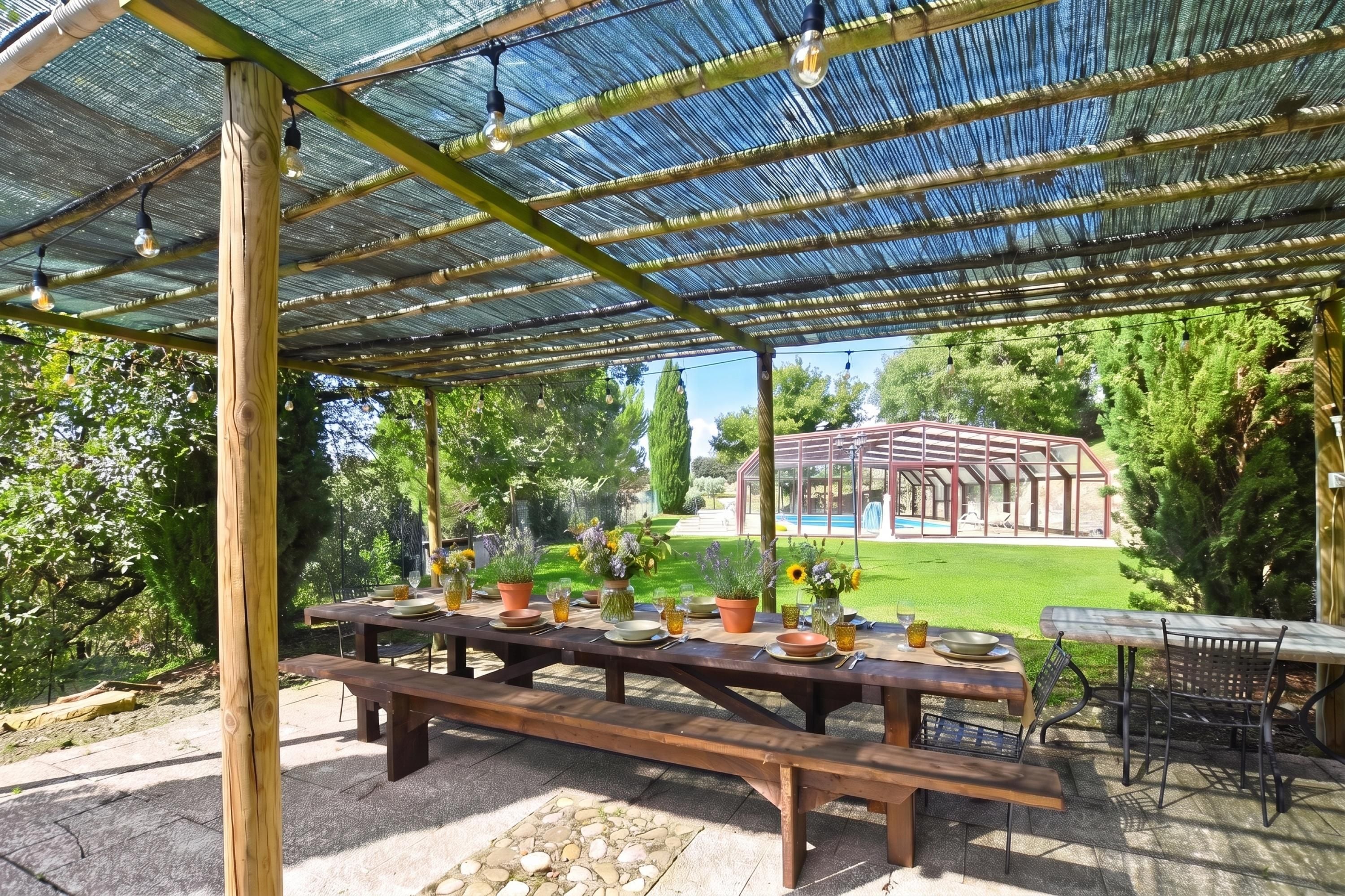 Une terrasse extérieure dotée d’un espace salon abrité, d’une table dressée pour le repas et d’une piscine en arrière-plan.