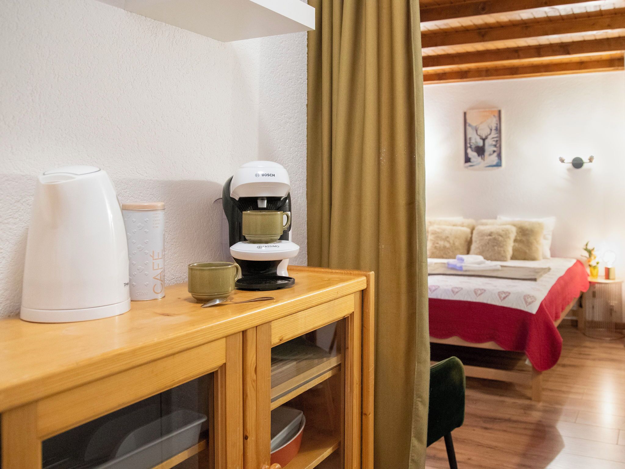 A cozy room with a wooden desk, a coffee maker, and a bed with a red blanket.
