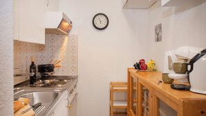 Eine kleine Küche mit Herd, Spüle und Holzschrank. Eine Uhr ist an der Wand befestigt und eine Kaffeemaschine steht auf der Arbeitsfläche.