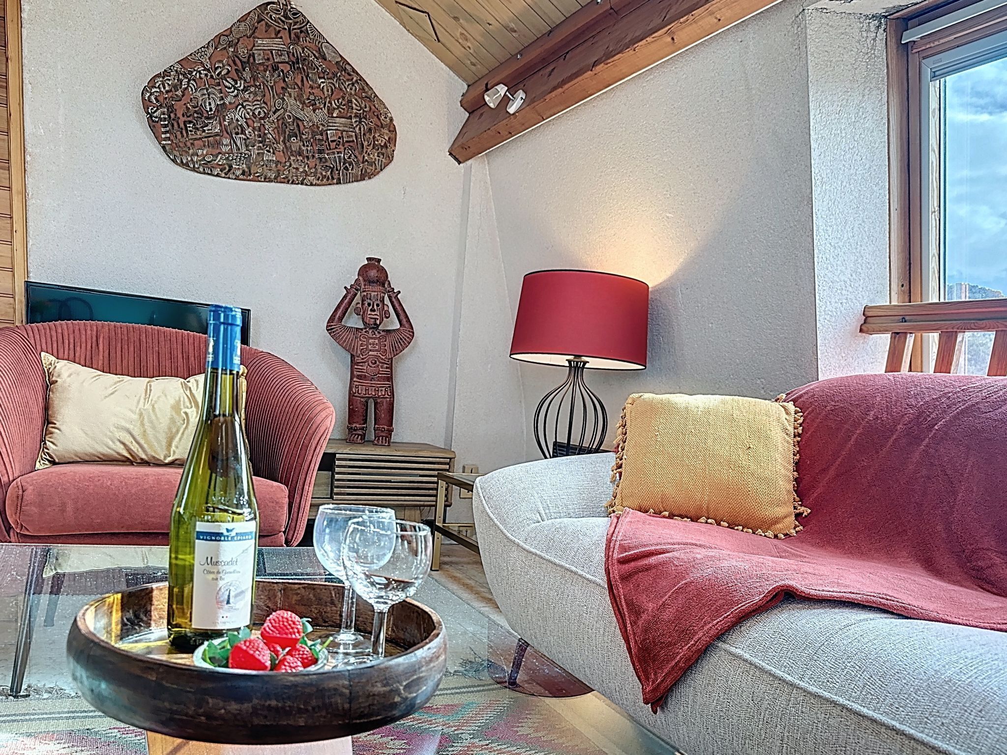 Un accogliente soggiorno con soffitto in legno, una lampada rossa, un elemento decorativo a parete e un divano con una coperta rossa.