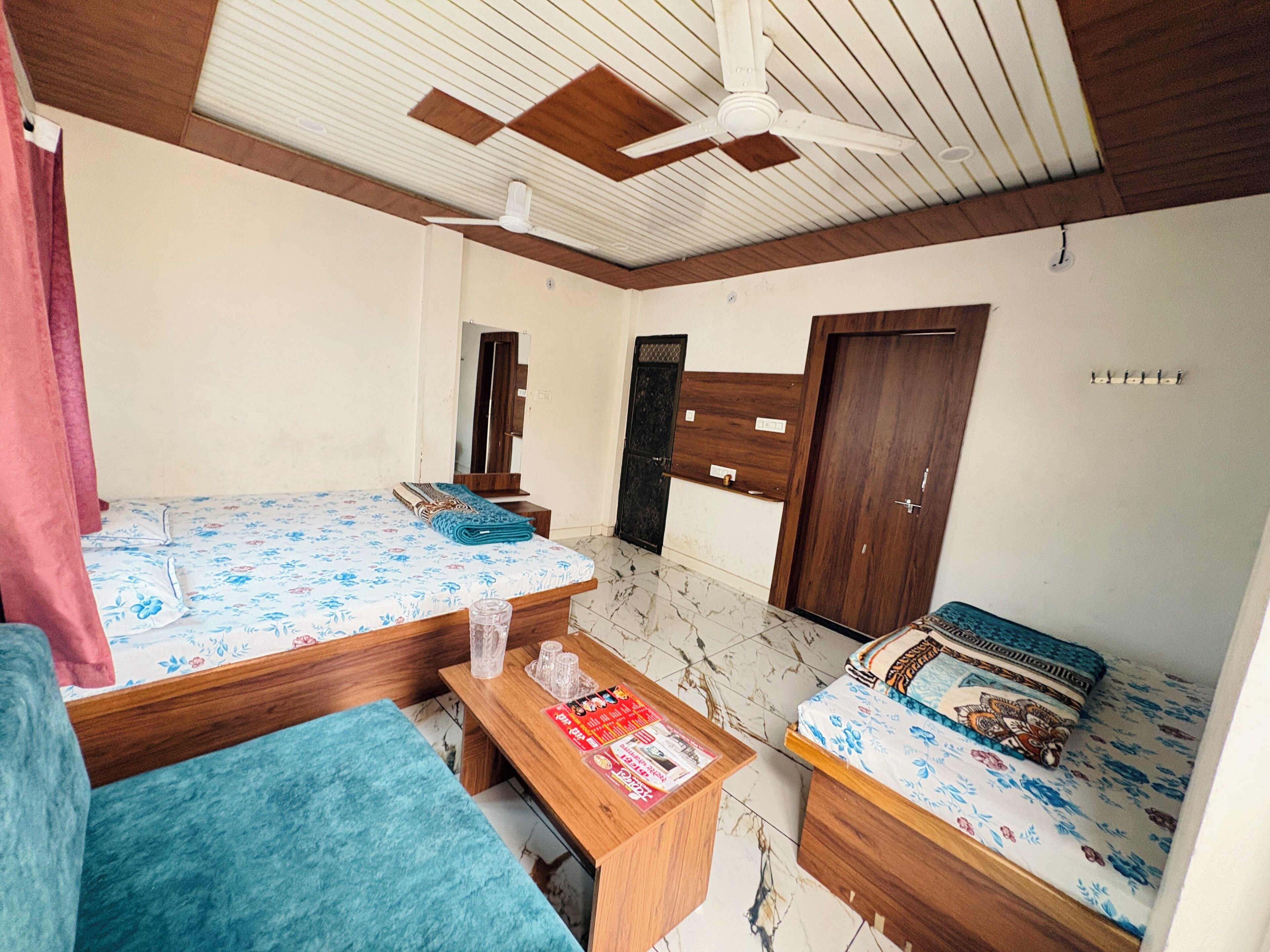 A room with two beds, a wooden ceiling fan, a wooden door, and a tiled floor.