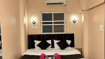 Una habitación de hotel con una cama, un ventilador de techo, un equipo de aire acondicionado y dos luces fijadas a la pared.