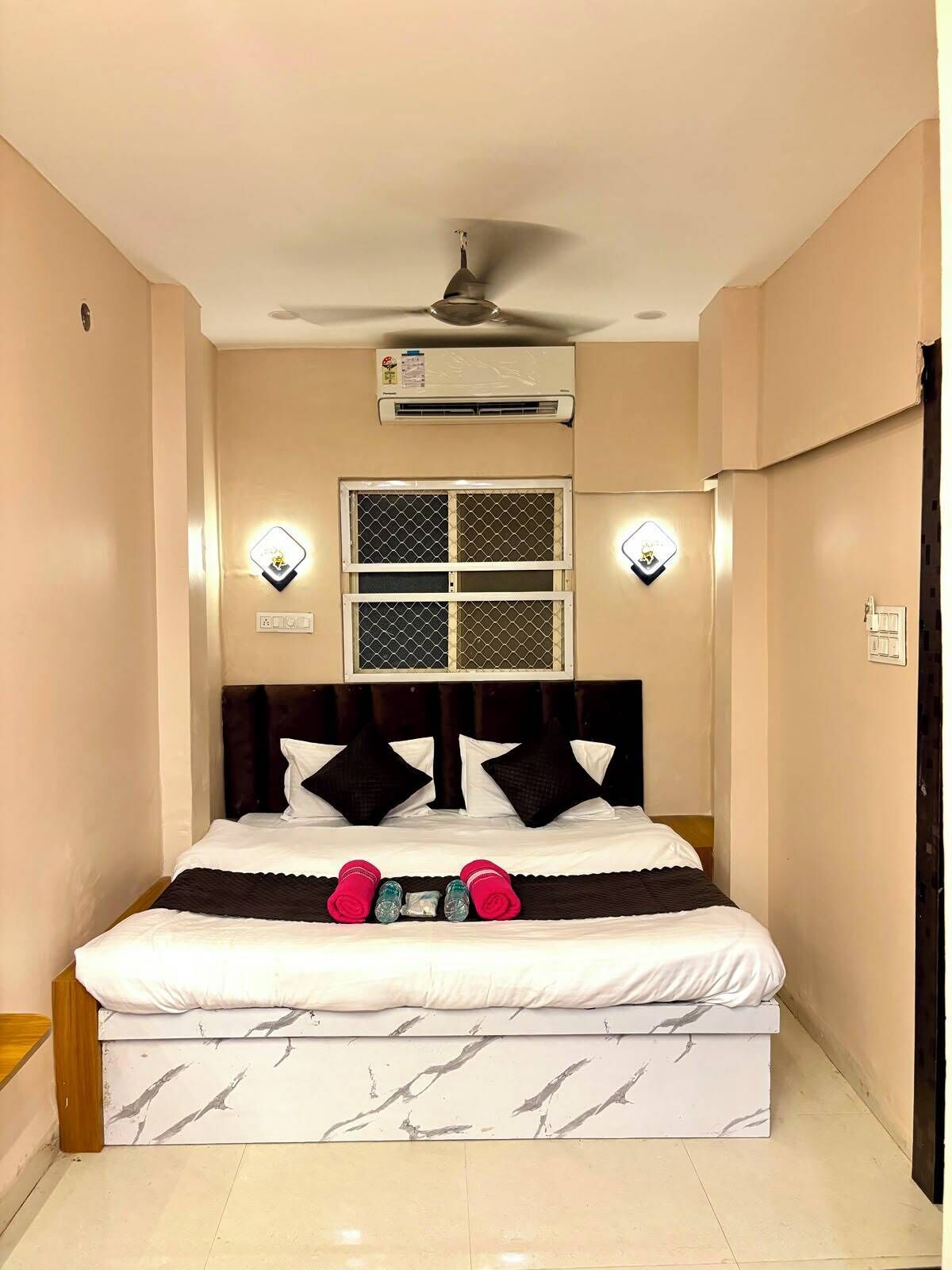 Ein Hotelzimmer mit einem Bett, einer Klimaanlage, einem Deckenventilator und zwei Wandleuchten.