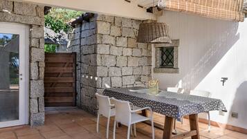Une terrasse avec un mur en pierre, une porte en bois, une table avec des chaises et un panier suspendu.
