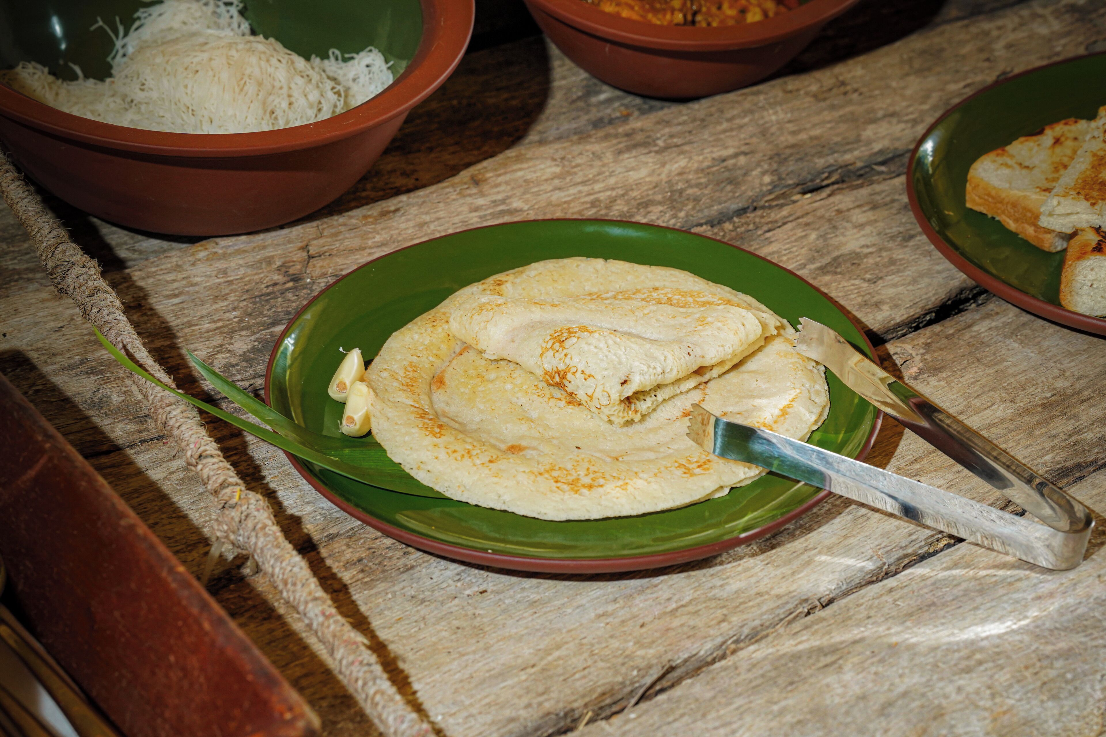 A wooden table with a green plate holding a flatbread and a knife.