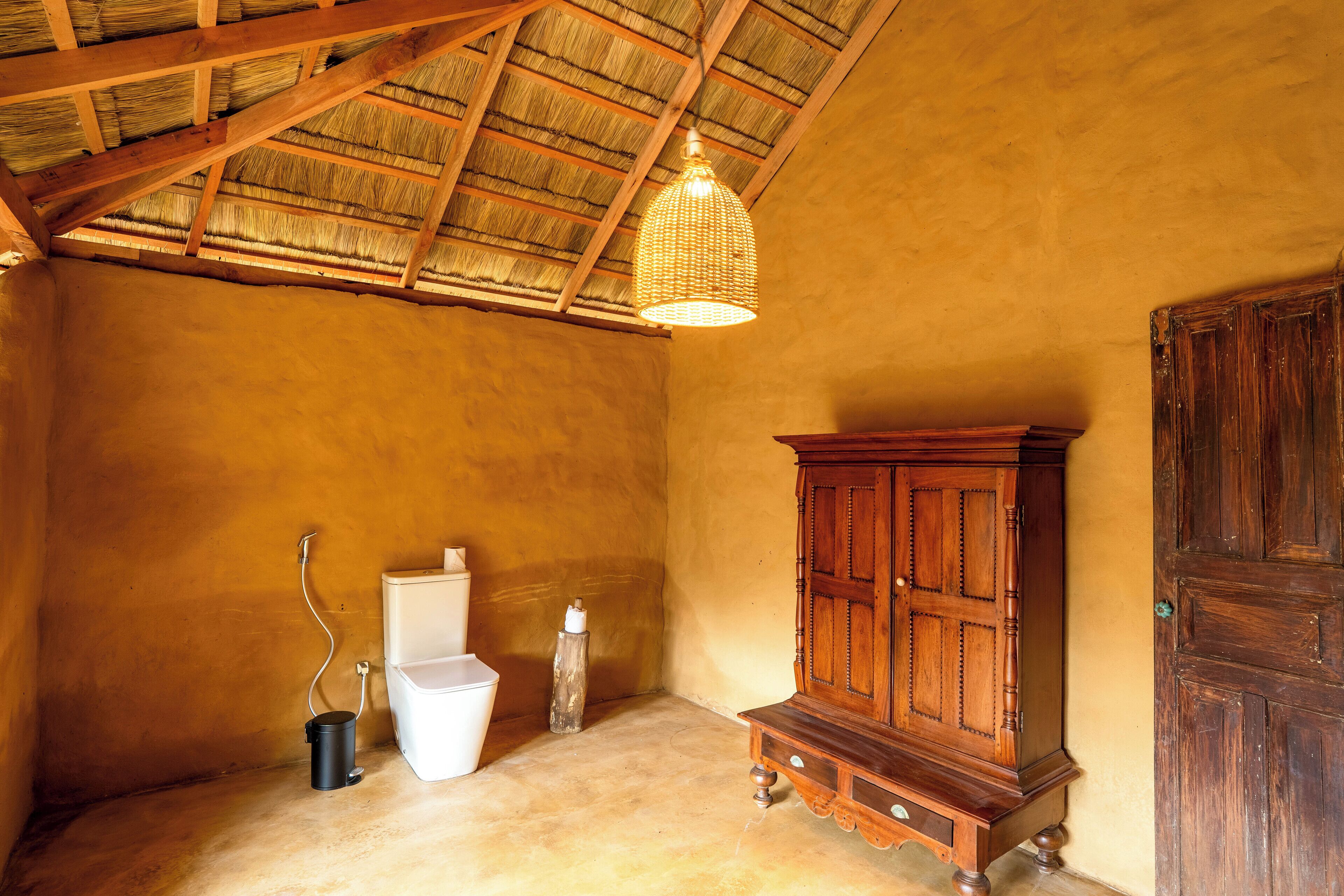 A rustic bathroom with a wooden cabinet, a white toilet, and a hanging light fixture.