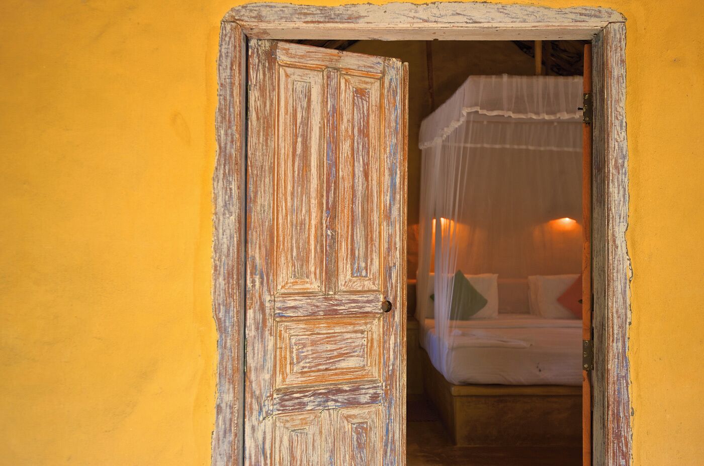 Een houten deur in landelijke stijl die leidt naar een kamer met een bed en hemelbed.