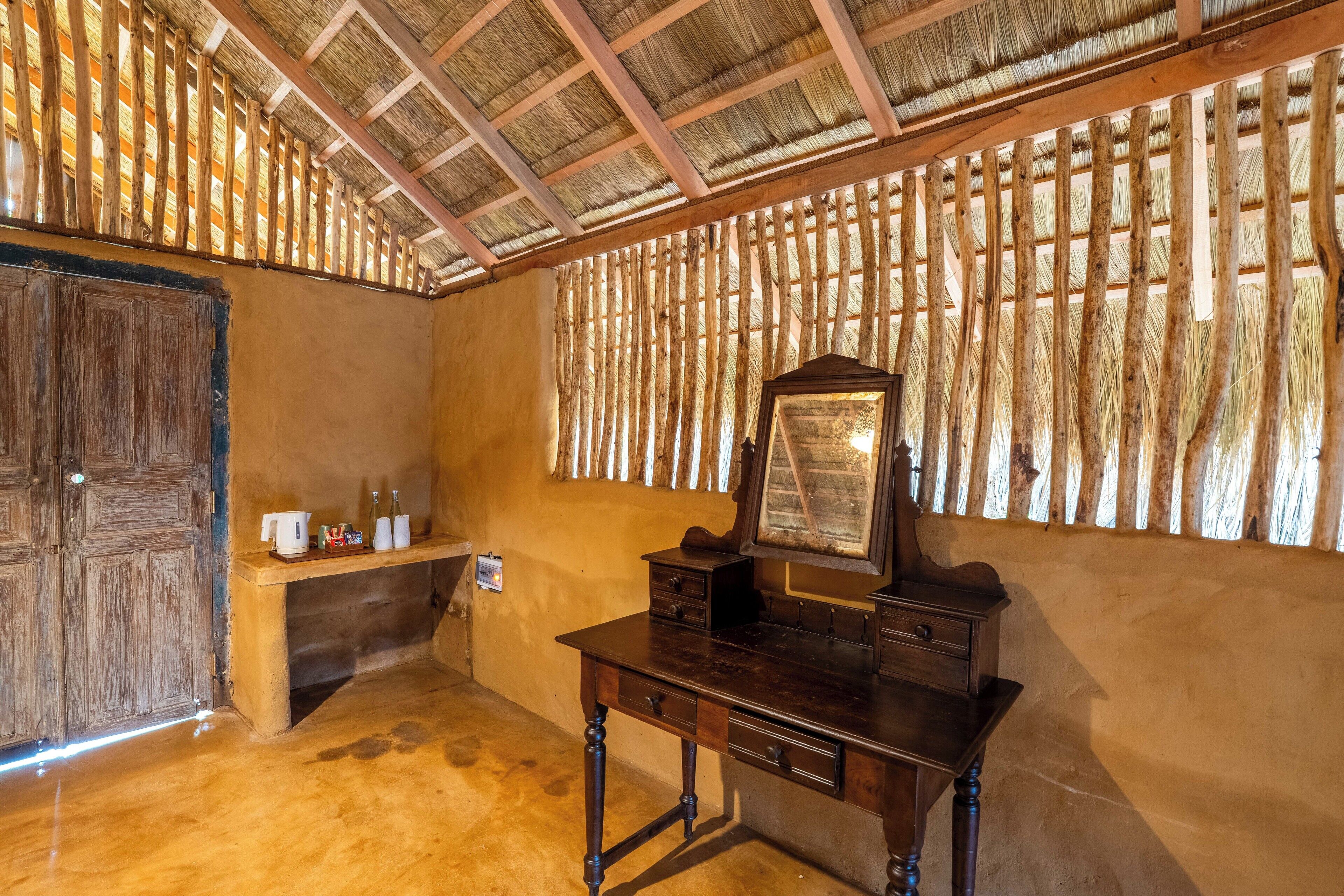 Quarto rústico com escrivaninha de madeira, espelho e prateleira com artigos de higiene pessoal.