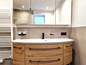 Ein modernes Badezimmer mit einem weißen Waschbecken, Holzschränken und einem großen Spiegel darüber.