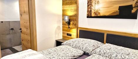 A bedroom with a wooden headboard, a bed with patterned bedding, a nightstand with a lamp, and a painting of a forest scene.