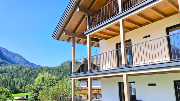 Un edificio de varios pisos con balcones, vistas despejadas del bosque y las montañas circundantes, y un jardín bien cuidado.