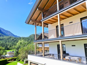 Un immeuble à plusieurs étages doté de balcons, offrant une vue dégagée sur la forêt et les montagnes environnantes, et comprenant un jardin bien entretenu.