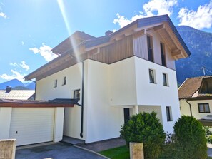 Ein modernes, zweistöckiges Haus mit Garage, einem geneigten Dach und Blick auf Berge im Hintergrund.