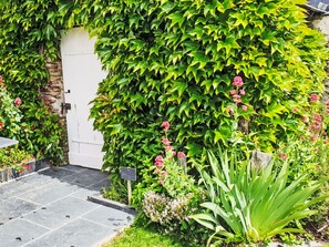 A garden with a white door, lush green foliage, and various plants. - Les Goganes by Interhome (Champtocé-sur-Loire)