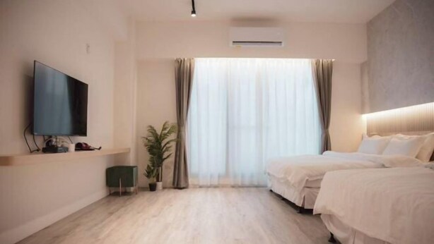 Ein Hotelzimmer mit einem großen Bett, einem an der Wand befestigten Fernseher und einem Fenster mit Vorhängen.