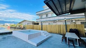 Ein Poolbereich auf dem Dach mit Tisch und Stühlen, einer Holzumzäunung und einem Gebäude im Hintergrund.