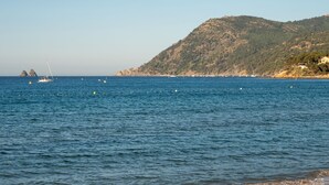 Une plage aux eaux calmes, avec des bateaux et un paysage vallonné en arrière-plan.