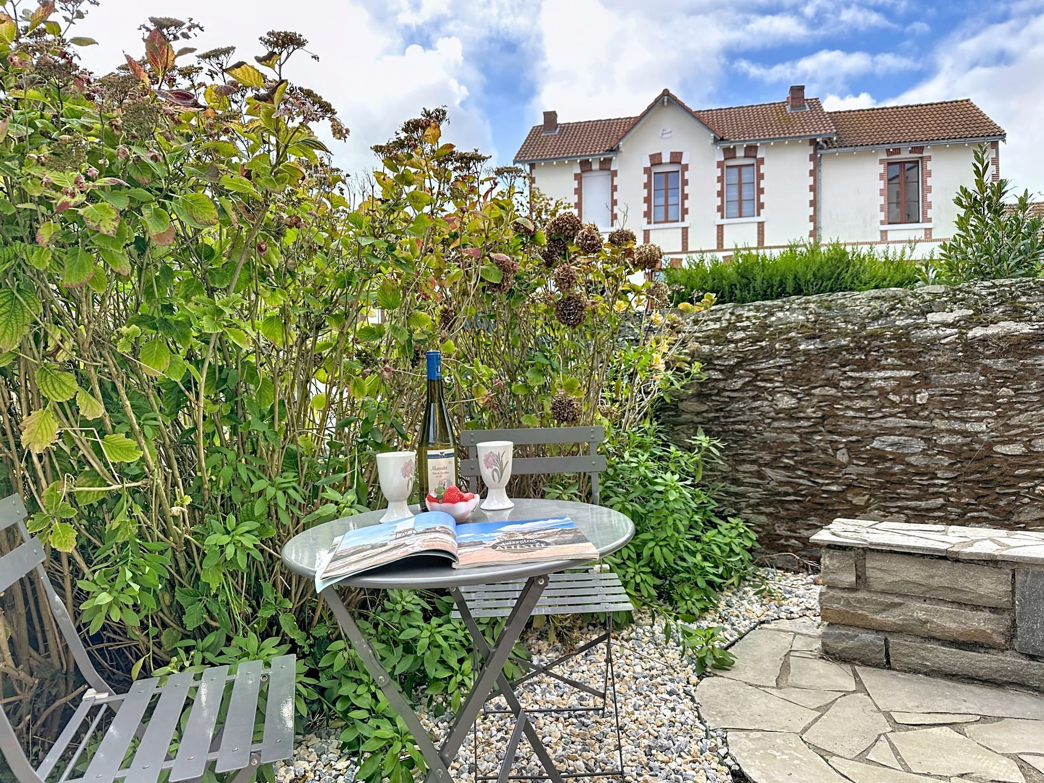 Un coin de jardin aménagé avec une table, un banc et une bouteille de vin.