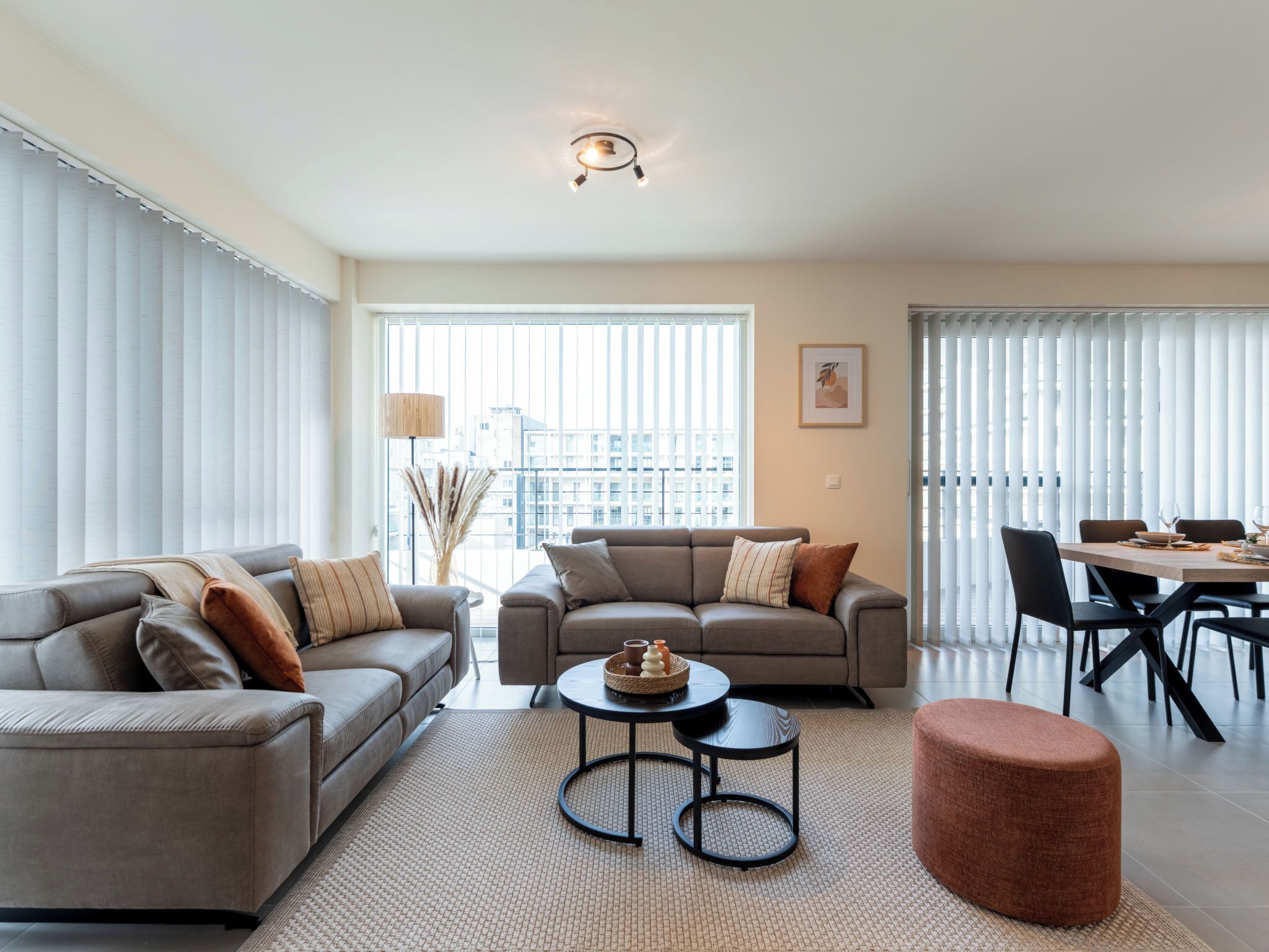 A modern living room with a sofa set, a round coffee table, and a dining area with a table set for two.