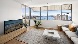 Una sala de estar moderna con un televisor grande, un sofá, una mesa de centro y vistas al mar a través de amplios ventanales.