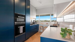 Una cocina moderna con armarios azul oscuro, una isla grande con taburetes y vistas a la ciudad a través de la ventana.