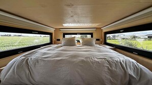 A bedroom with a large bed, two windows, and a view of a field.