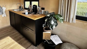 A compact kitchen with a wooden countertop, black cabinets, and a large window with curtains.