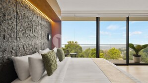 Een moderne slaapkamer met een groot bed, een accentmuur van steen en uitzicht op een groen landschap door grote ramen.