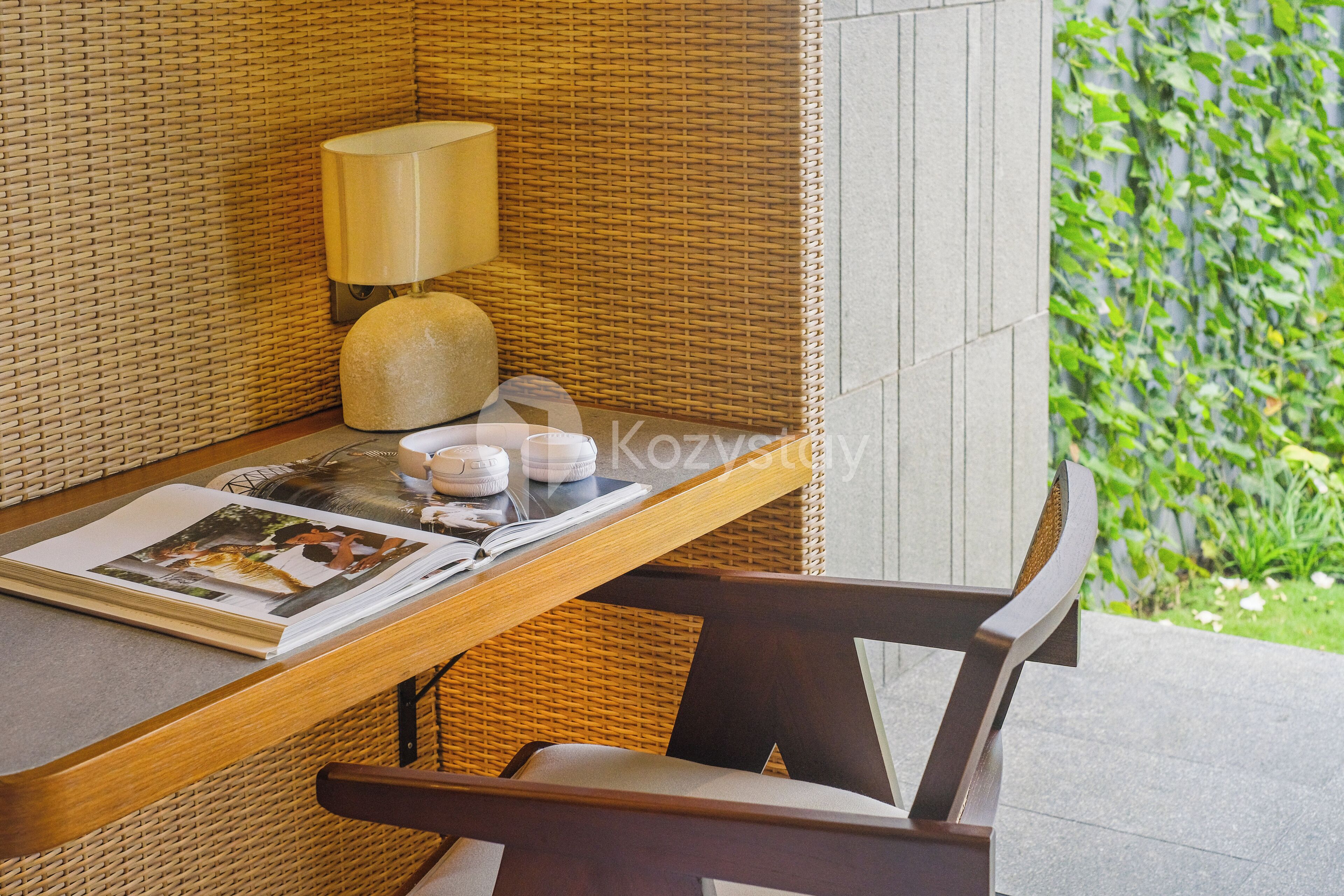 Una silla de mimbre y una mesa con una lámpara, un libro y un pequeño objeto decorativo.