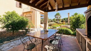 An outdoor patio with a table and chairs, surrounded by greenery and a building with a tiled roof. - Villa Athena with private pool - My Rental Homes (Castelvetrano)