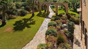 A stone pathway leading to an arched structure in a well-maintained garden with a clear sky and distant mountains. - Villa Athena with private pool - My Rental Homes (Castelvetrano)