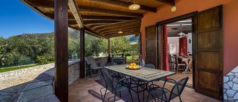 A covered patio with a table and chairs, a wooden ceiling, and a view of greenery and mountains.