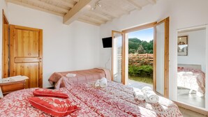 A bedroom with a large bed, a wooden door, and a view of a garden through an open door. - Mugello House With Pool (Vicchio)