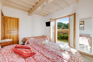 A bedroom with a large bed, a wooden door, and a view of a garden through an open door. - Mugello House With Pool (Vicchio)