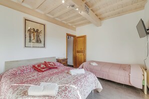 A bedroom with a large bed, a smaller bed, a wooden door, a TV, and a painting on the wall. - Mugello House With Pool (Vicchio)